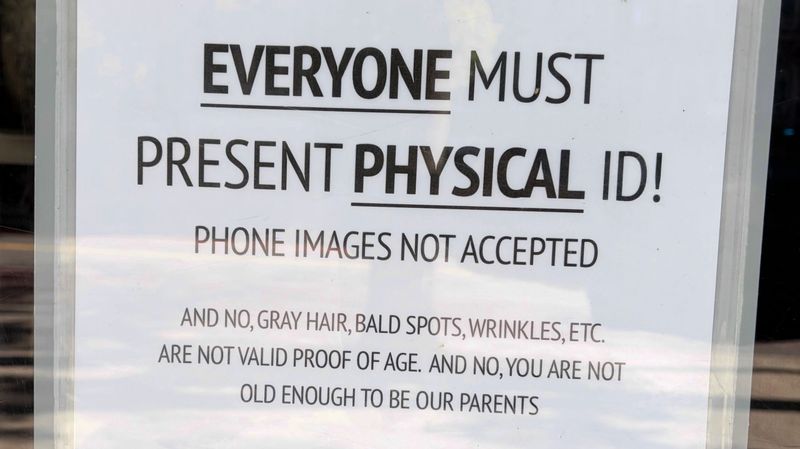 A handwritten sign reading: Everyone must present physical ID! Phone images not accepted. And no, gray hair, bald spots, wrinkles, etc. are not valid proof of age. And no, you are not old enough to be our parents.